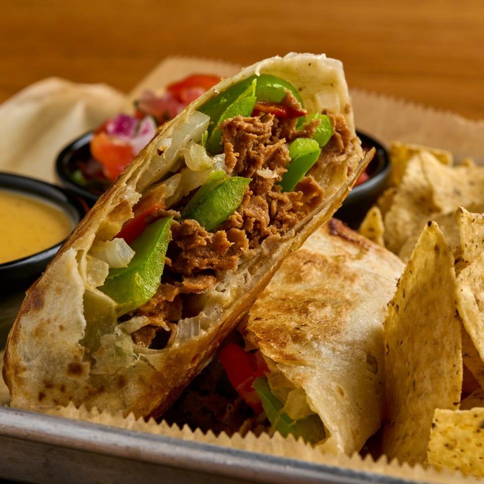 Two Salsaria's burritos, one cut open, filled with meat, onions, and peppers, served with chips and dip.