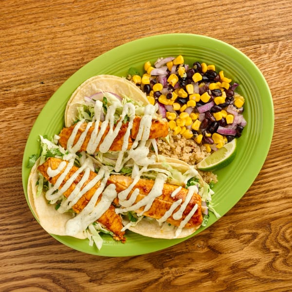 Two fish tacos with crema, shredded cabbage, and red onion, served with corn and black bean salsa.