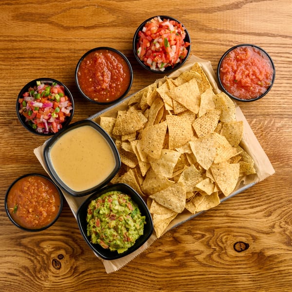 A tray of Salsaria's tortilla chips with bowls of salsa, pico de gallo, guacamole, and queso dip.
